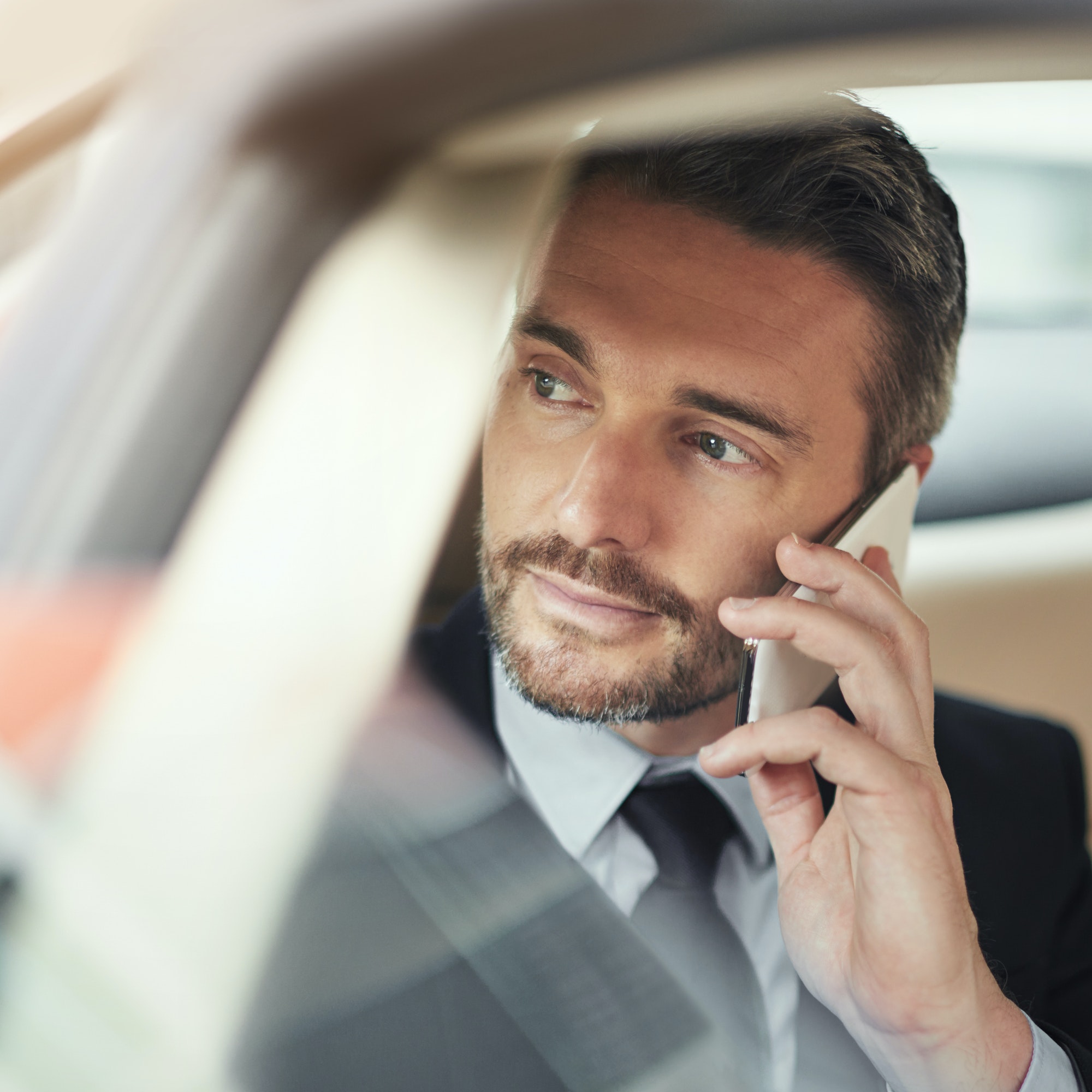 Shot of a businessman using his phone while traveling in a car